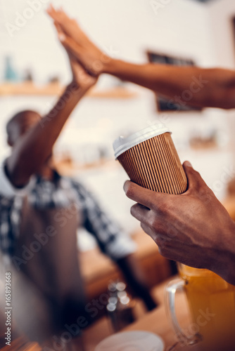 african american barista giving highfive to client with disposable cup in coffee shop