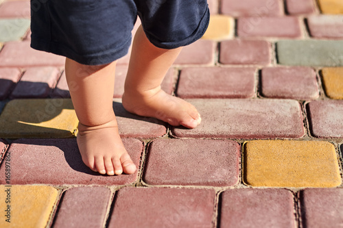 Baby legs barefoot on patterned paving tiles, cement brick floor background