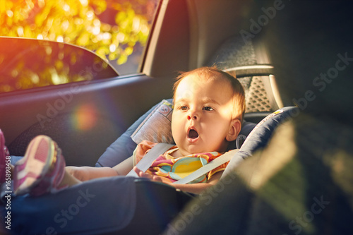 Close Up cute baby sitting in modern car seat. Child new born traveling safety on the road. Safe way to travel fastened seat belts in a vehicle with young kids. Trip with an infant.