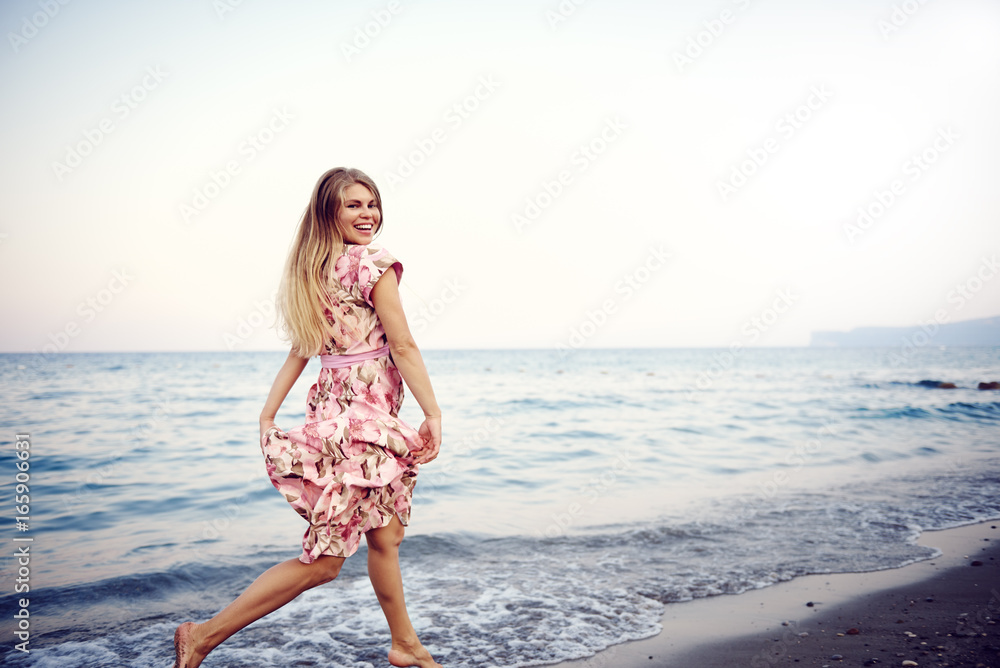Happy young woman in beautiful dress running on ocean beach at sunset. 