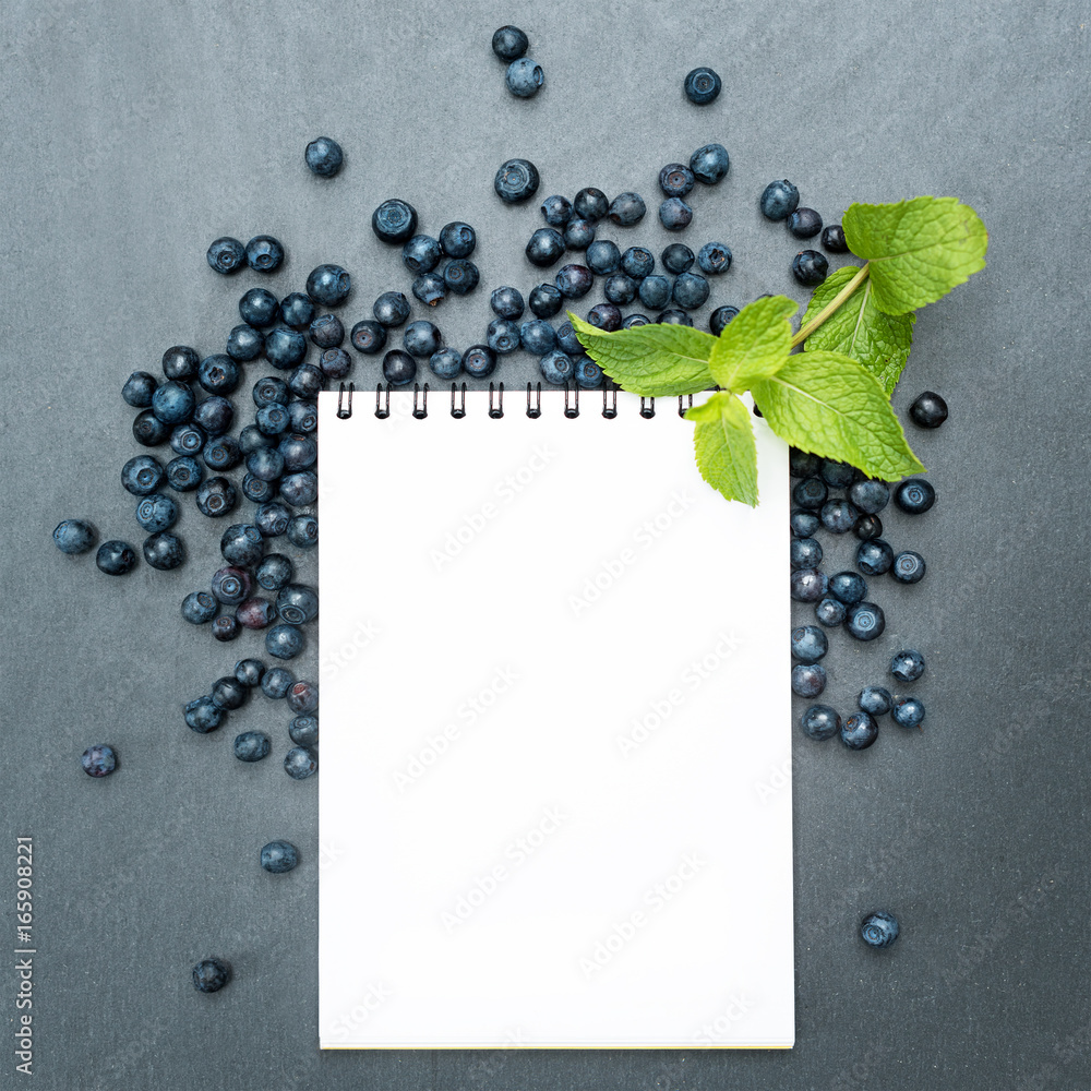 Fototapeta premium Blueberries, mint leaves and notepad for writing notes or resolutions, concept of sport, diet, slimming, detox, healthy lifestyles and nutrition. Mock up, space for text.
