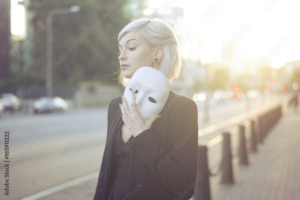 Young blond woman taking off a mask. Pretending to be someone else concept. outdoors on sunset. Young blond woman taking off a mask. Pretending to be someone else concept. outdoors on sunset.
