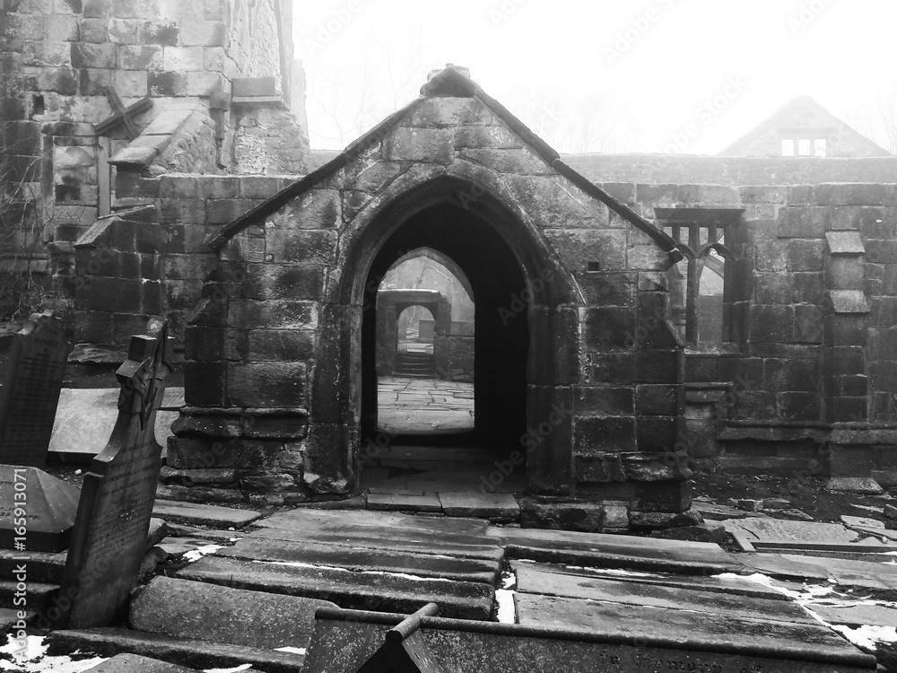 Fototapeta premium ruined medieval church in heptonstall yorkshire in fog and mist with patches of snow on the ground on the graveyard