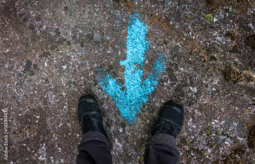 Tableau sur toile Woman standing at a blue painted direction arrow on the ground