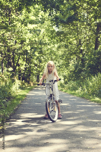 Child blond girl riding a bicycle on a bike path in summer © Petr Bonek