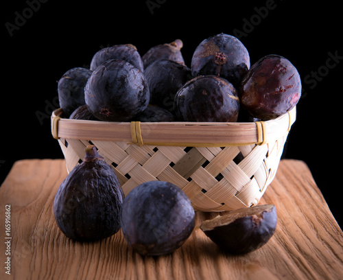 Fresh purple figs in wicker light basket on the rustic board. Cuted figs on rustic table. Horizontal version. photo