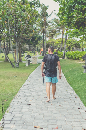 Rear view of man with backpack walking in the beach park of Nusa Dua  Bali island  Indonesia.