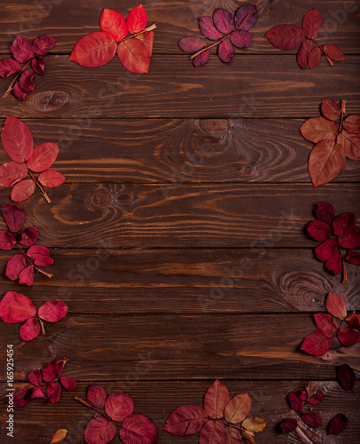 Flat lay frame of autumn crimson leaves on a dark wooden background.