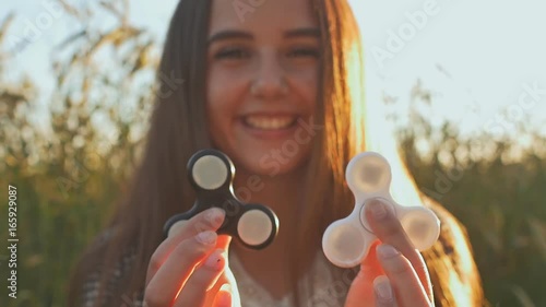 Young girl holding and rotates in the rays of the evening sun a white and black fidget spinners outdoors. photo