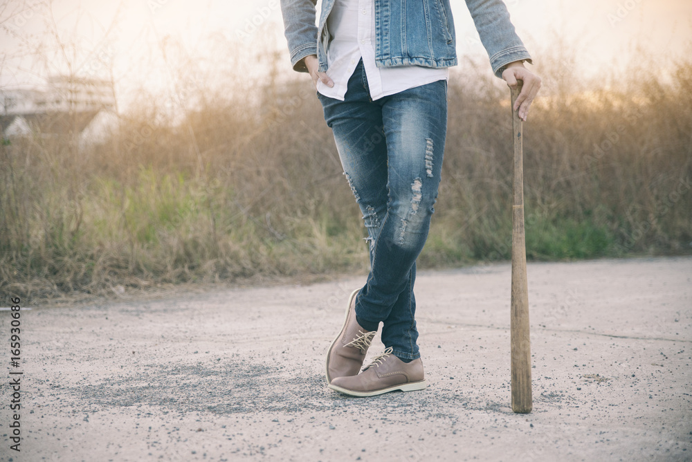 Handsome young man (fashion man) in smart casual wearing blue jeans,white  shirts and leather boots,standing on concrete floor.Aggressive Man holding  baseball bat with sunset background.Fashion concept Stock Photo | Adobe  Stock