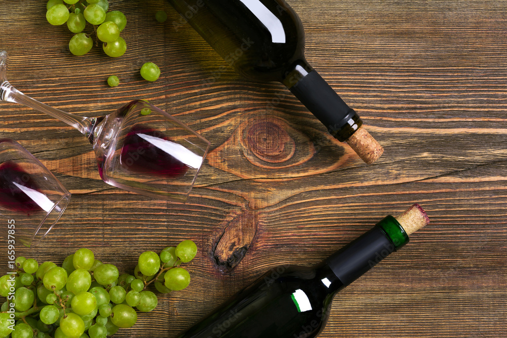 Obraz premium Red and white wine bottles, grape and glasses over wooden table. Top view with copy space