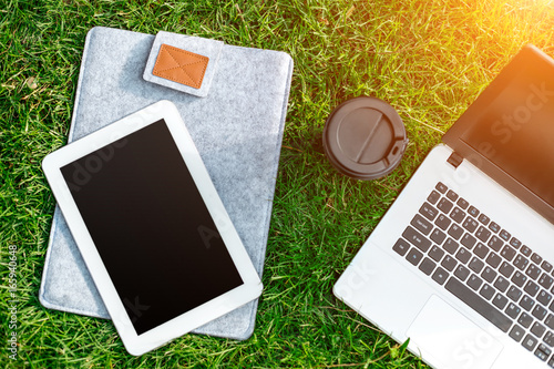 Fototapeta Naklejka Na Ścianę i Meble -  Laptop computer on green grass with coffee cup and tablet in outdoor park