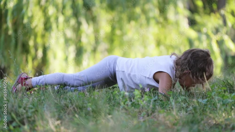 Sporty cute little girl doing walking plank exersice on the meadow in the park.