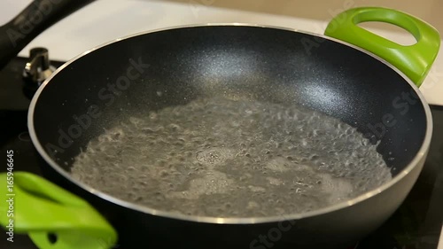 Putting boiling water for cooking in a wok on a stove photo