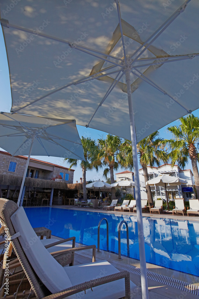 Relaxing pool at small hotel with umbrellas chaise-longue and surrounded with palms