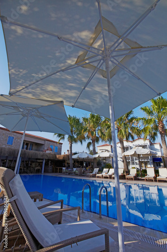 Relaxing pool at small hotel with umbrellas chaise-longue and surrounded with palms © Ekaterina