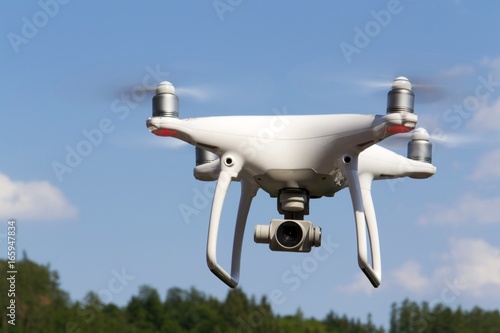 White drone quadrocopter with camera flying over forest