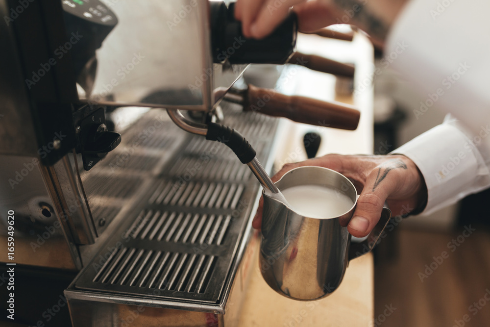 Barista preparing coffee at the counter in coffee shop. Close up man hand whipping milk for coffee by coffee machine in restaurant