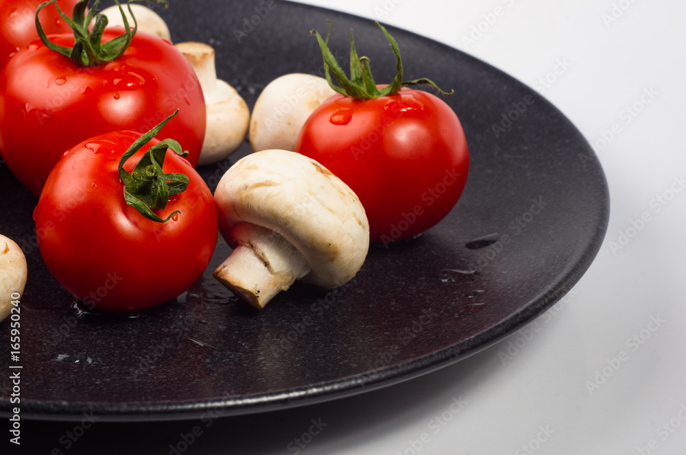 fresh tomatoes and mushrooms - champignons on black plate fresh tomatoes and mushrooms - champignons on black plate