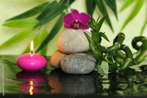 galets disposés en mode de vie zen au centre avec une orchidée au sommet avec des tiges de bambou et une bougie rose allumée 