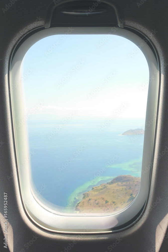 Looking out airplain window seat at exotic tropical coast of islands and blue turquoise colored ocean water while arriving at Flores, Indonesia