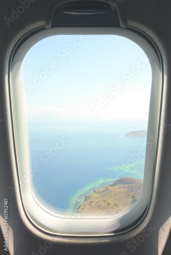 Looking out airplain window seat at exotic tropical coast of islands and blue turquoise colored ocean water while arriving at Flores  Indonesia