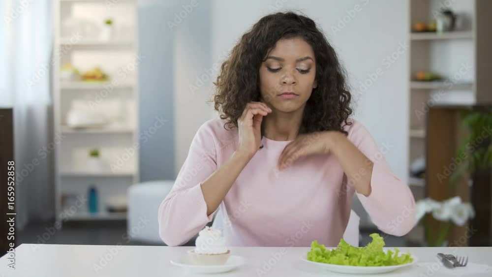 Beautiful biracial woman choosing between salad and sweets, health, choice Beautiful biracial woman choosing between salad and sweets, health, choice