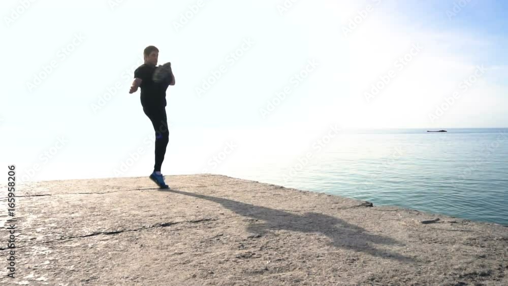 Young man does round house high kicks barefooted against sunrise in slow motion Young man does round house high kicks barefooted against sunrise in slow motion