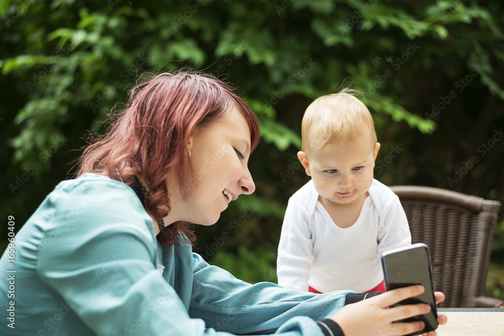 Young woman playing with her baby, showing something on her phone Young woman playing with her baby, showing something on her phone