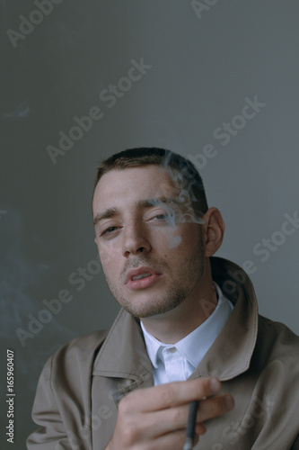 Fototapeta Naklejka Na Ścianę i Meble -  A handsome and lonely guy in a cloak with a cigarette