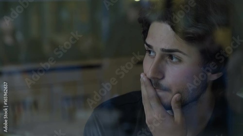 Closeup of stressed business man thinking and sitting near glass window into a pub people passing by