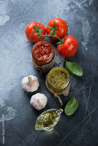 Red and green pesto sauces with cooking ingredients on a grey stone background, vertical shot, high angle view