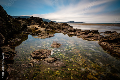 Tidepool along California coast with rocky shore and streaky clouds