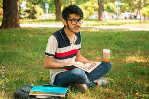 young student sitting on a lawn with coffee and books
