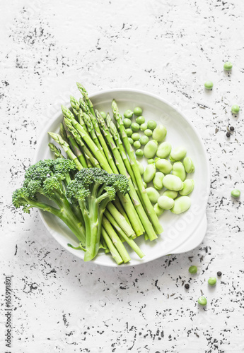Green vegetables - asparagus, broccoli, green beans and peas on a light background, top view