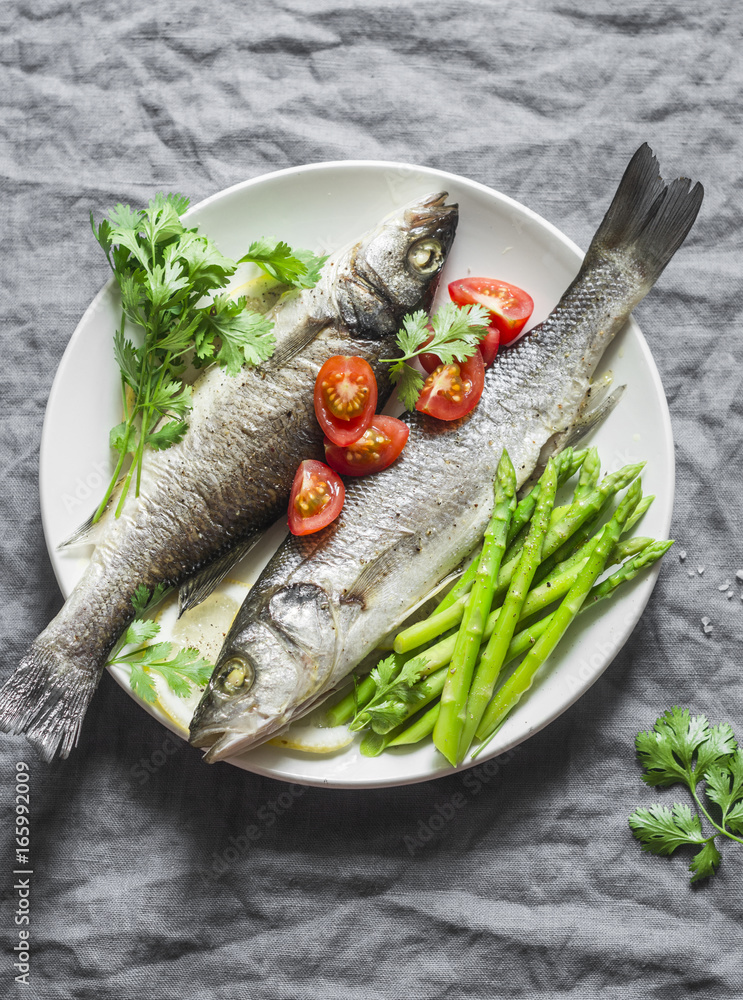 Baked sea bass with asparagus and tomatoes. Healthy diet food concept. On a gray background, top view Baked sea bass with asparagus and tomatoes. Healthy diet food concept. On a gray background, top view