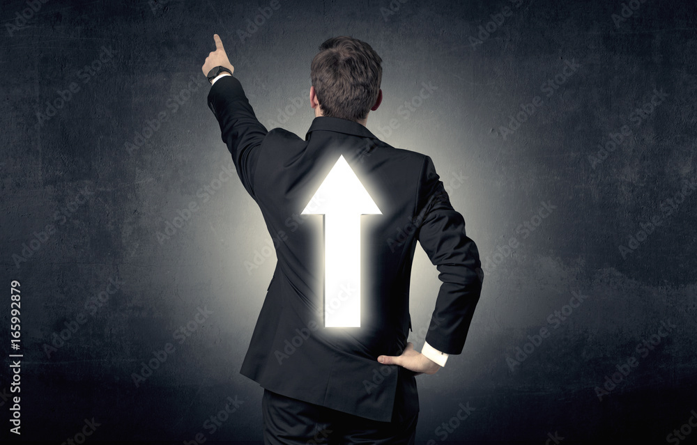 Young businessman standing with arrow on his back Young businessman standing with arrow on his back