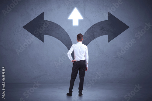 Businessman taking a decision while looking at arrows on the wall concept