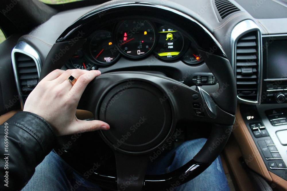 A man holds the steering wheel of a luxury car. Gold watch and a ring on his hand