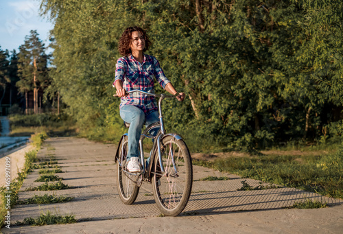 Young smiling woman rides a bicycle in the park on sunset background
