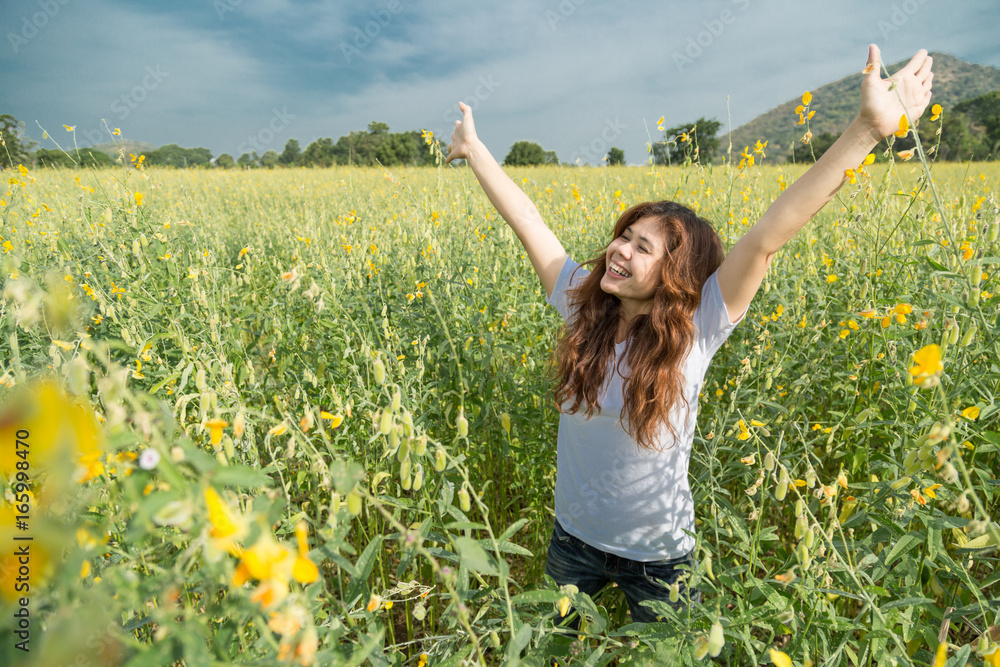 Naklejka premium asian women with slightly curly is raising arms to the sky in yellow field at summer, Thailand.