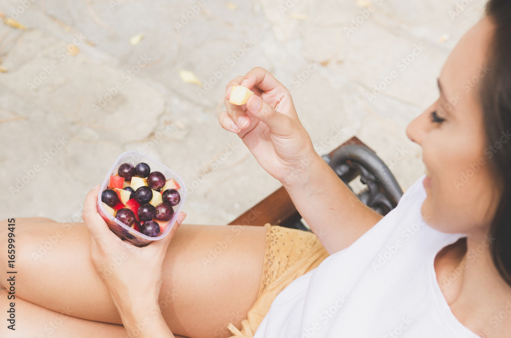 Naklejka premium Young woman holding delicious fruit salad with grapes. Outdoors summer.