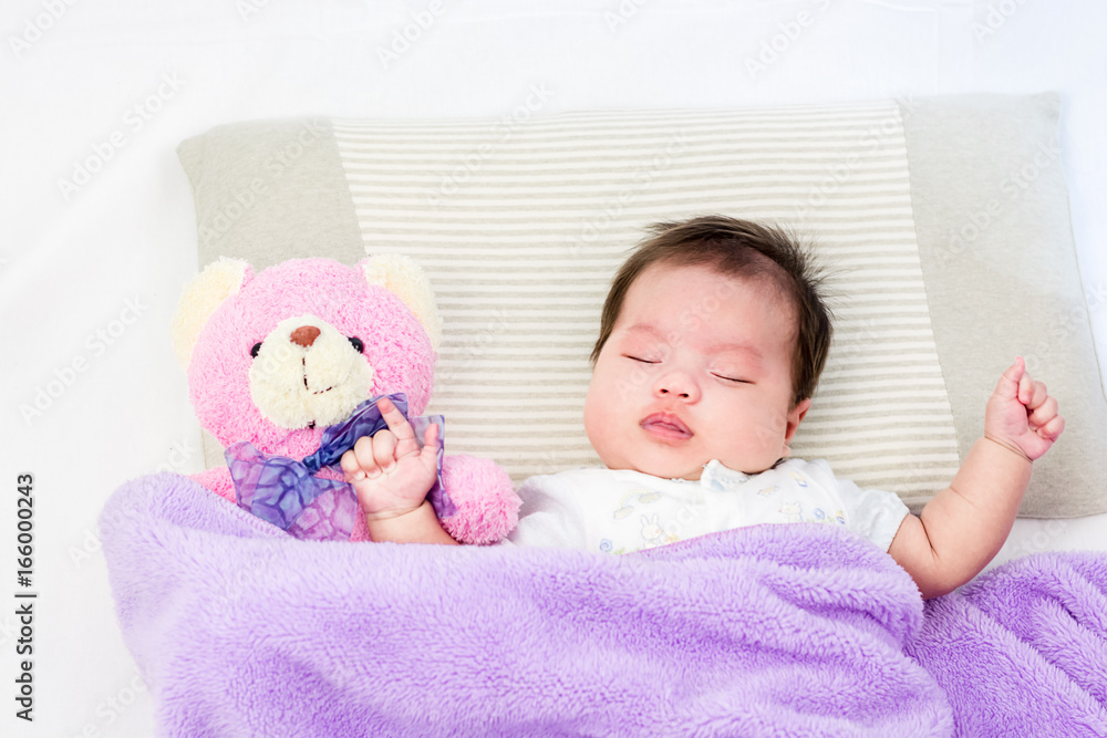 Portrait of sleeping baby  lying on a bed with bear doll