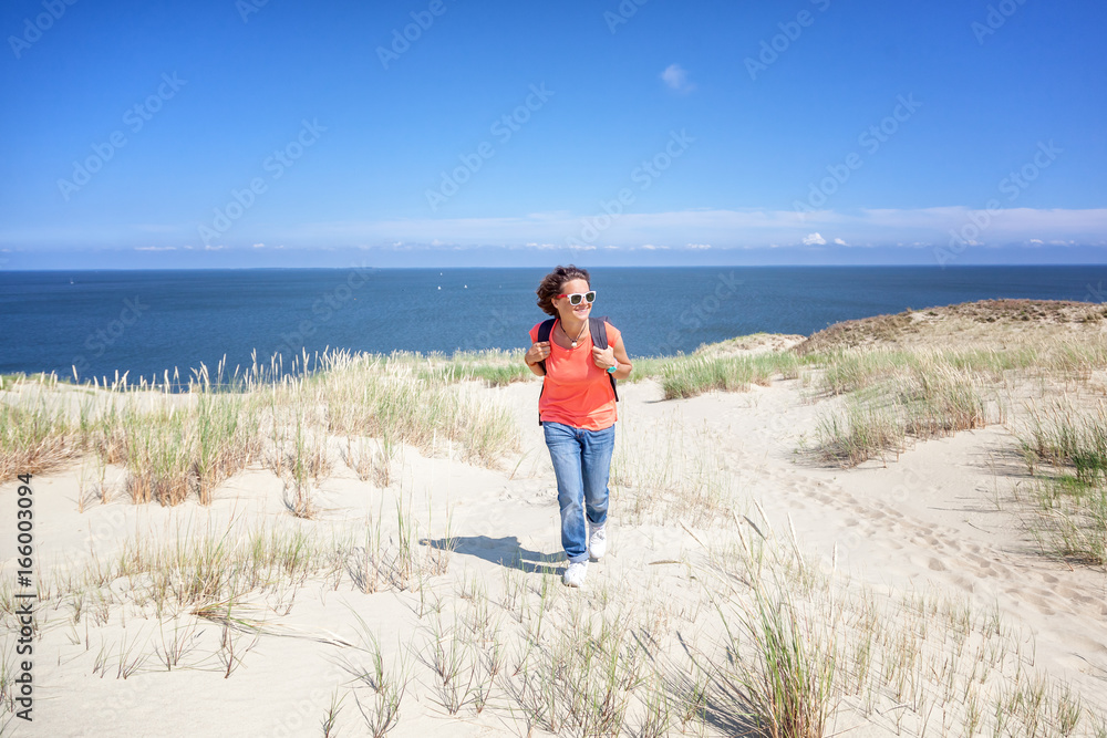 Beautiful young woman traveler with a backpack on the background of the sea and white dunes