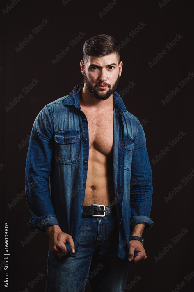 Young handsome muscular man with a beard, posing on a black background Young handsome muscular man with a beard, posing on a black background
