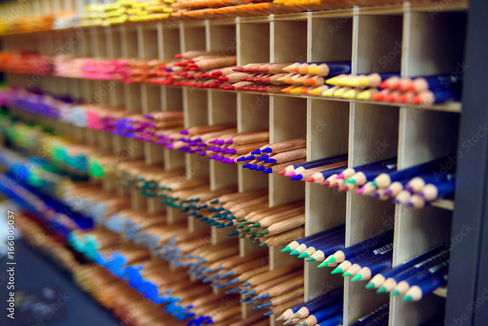 Multicolored pencils in art store in wooden cells closeup, selective focus. Artspace, workshop, creativity concept. Modern art.