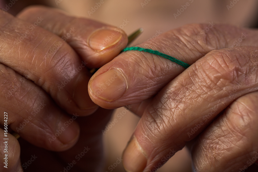 Fototapeta premium Knitting old hands and fingers holding knitting needle and woolen thread, grandmother prepares scarf or sweater, hands with wrinkles, retired hobbies in retirement, memories of grandmother, vintage 