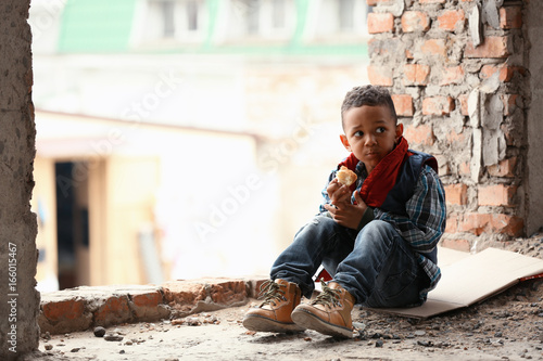 Fotografía Cute little boy sitting on floor with piece of bread in abandoned building