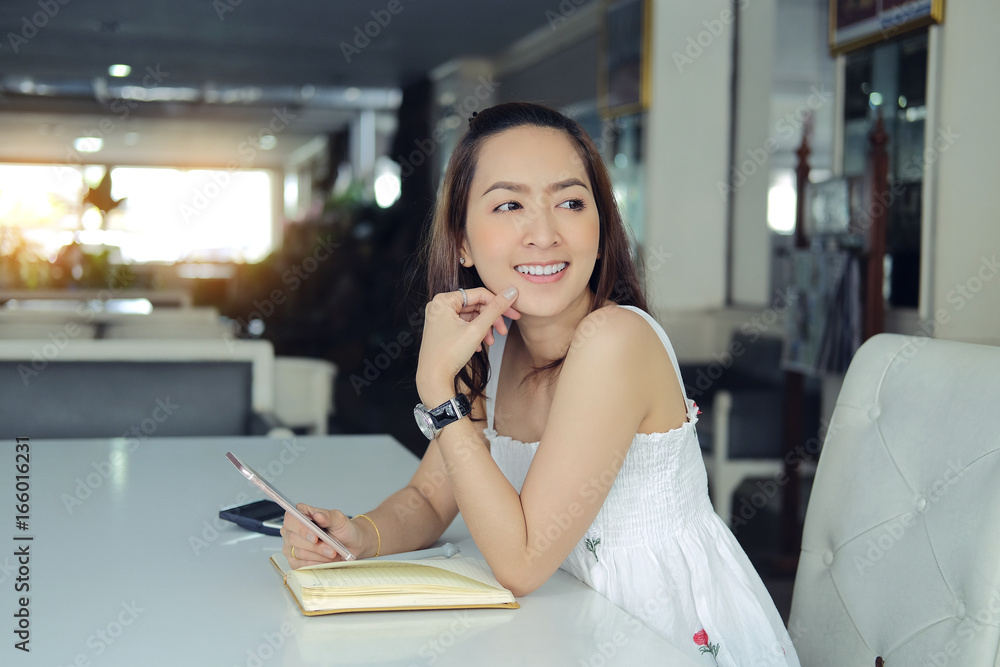 Portrait of smiling pretty young business woman in holding smartphone sitting on workplace Portrait of smiling pretty young business woman in holding smartphone sitting on workplace