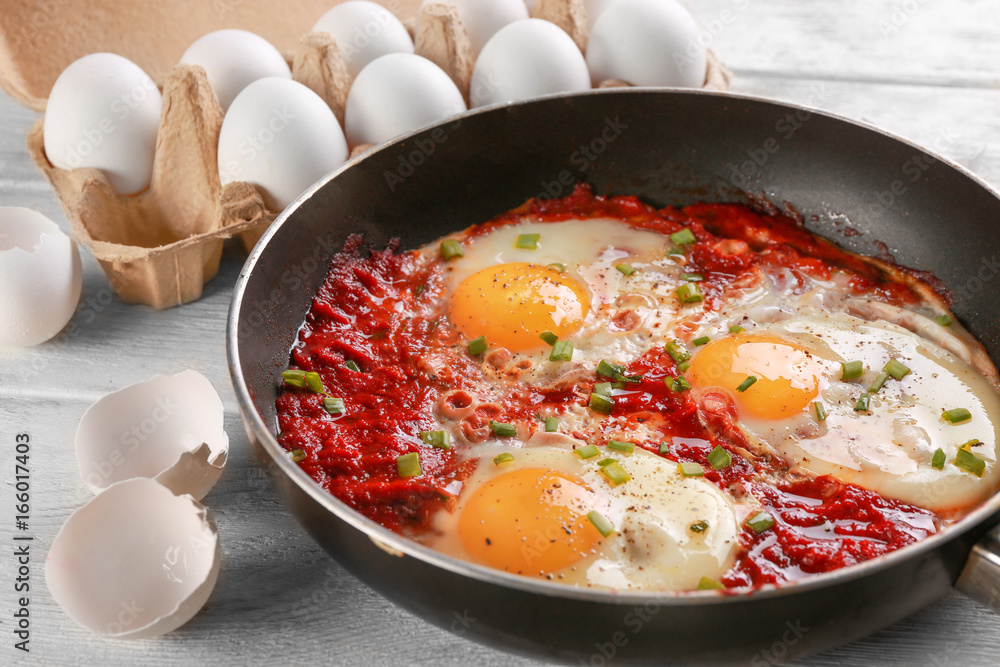 Wall Mural Frying pan with eggs in purgatory on wooden background